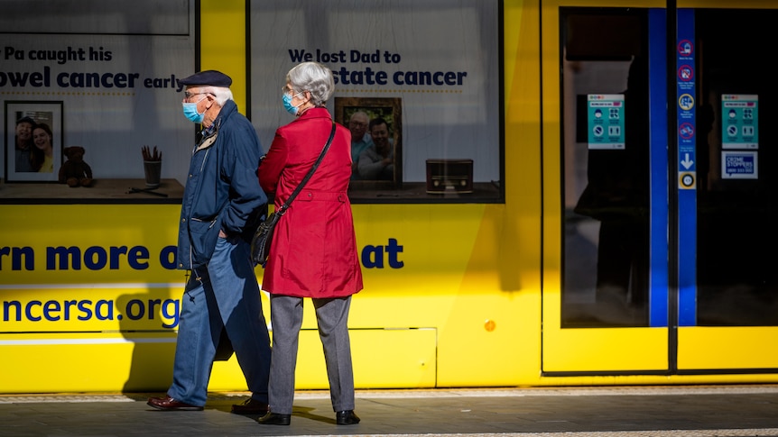 An elderly man and a woman at a tram stop next to a yellow tram