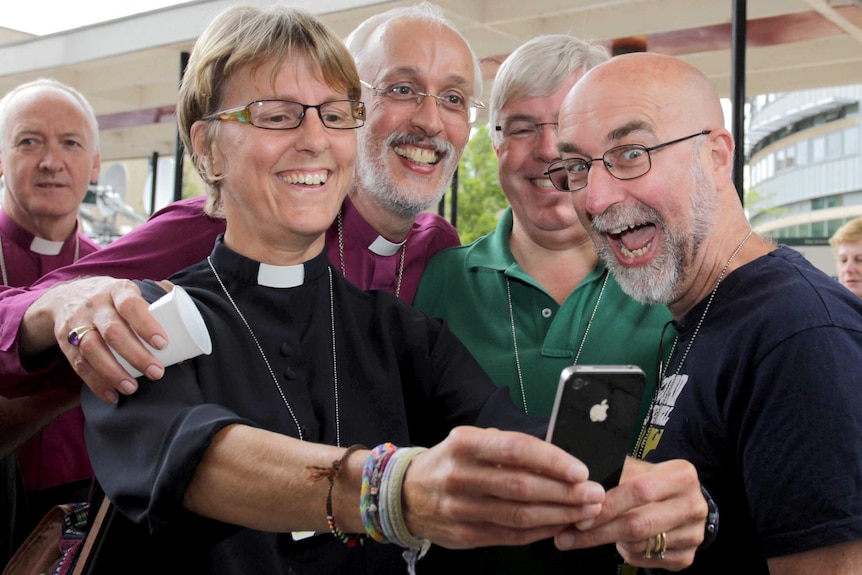 A female Church of England member of clergy takes a selfie with other members of clergy.