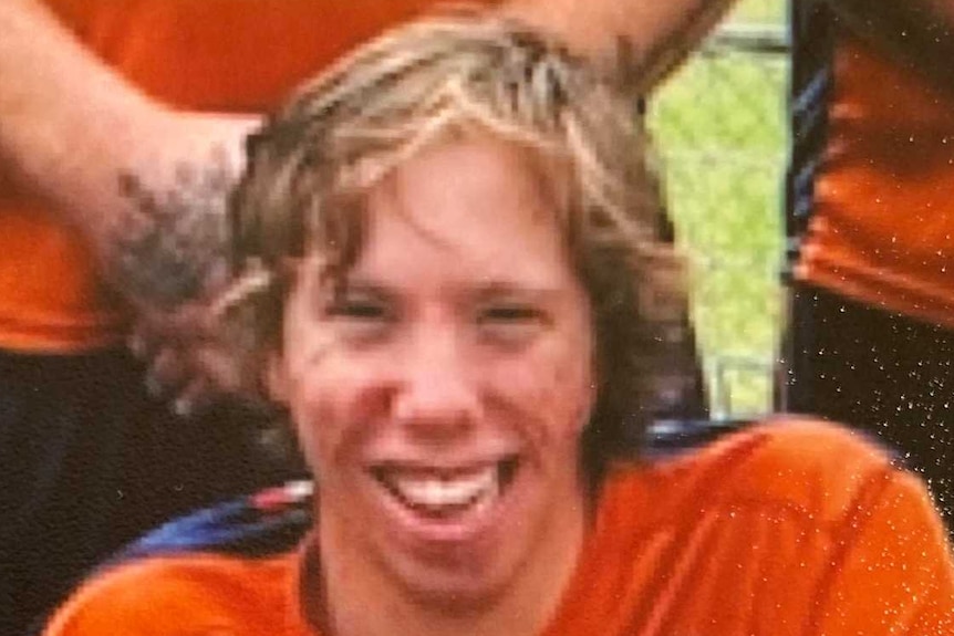 A man in an orange and black soccer top smiling at the camera
