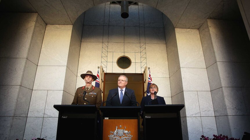 Australian officials stand behind lecterns in front of a grey wall