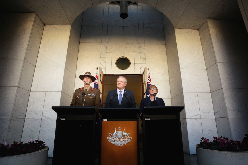 Australian officials stand behind lecterns in front of a grey wall