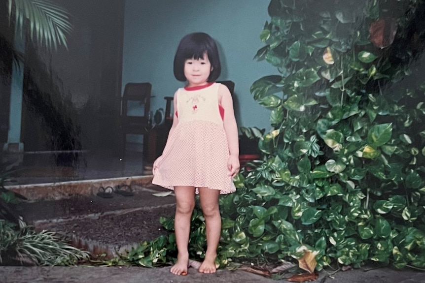 A three-year-old Chinese Indonesian girl standing in front of a house.