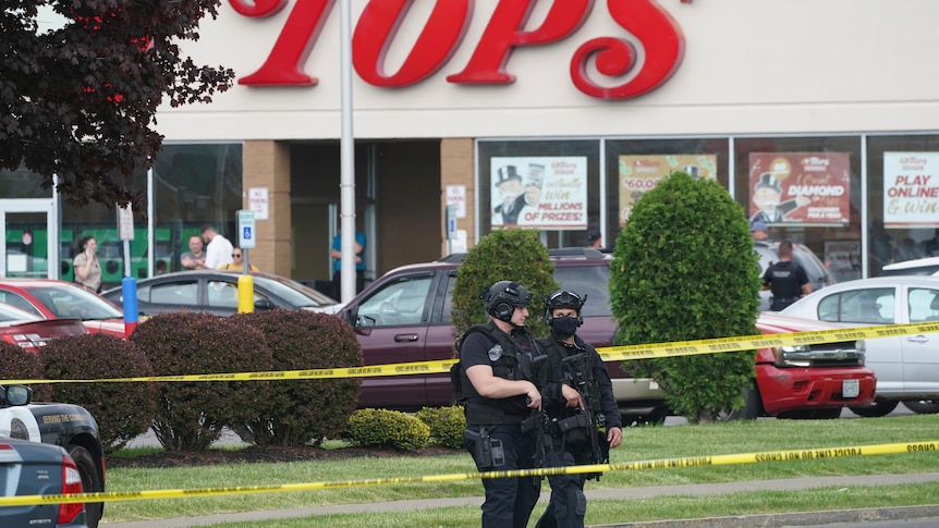 Two armed police stand outside a US supermarket surrounded by police tape