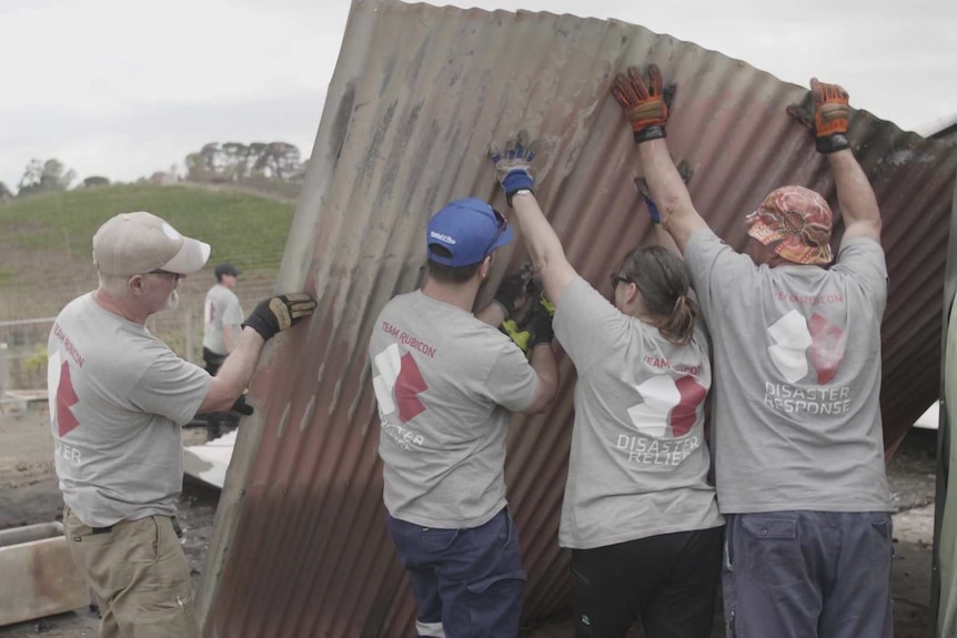 Members of Team Rubicon holding up a sheet of corrugated iron