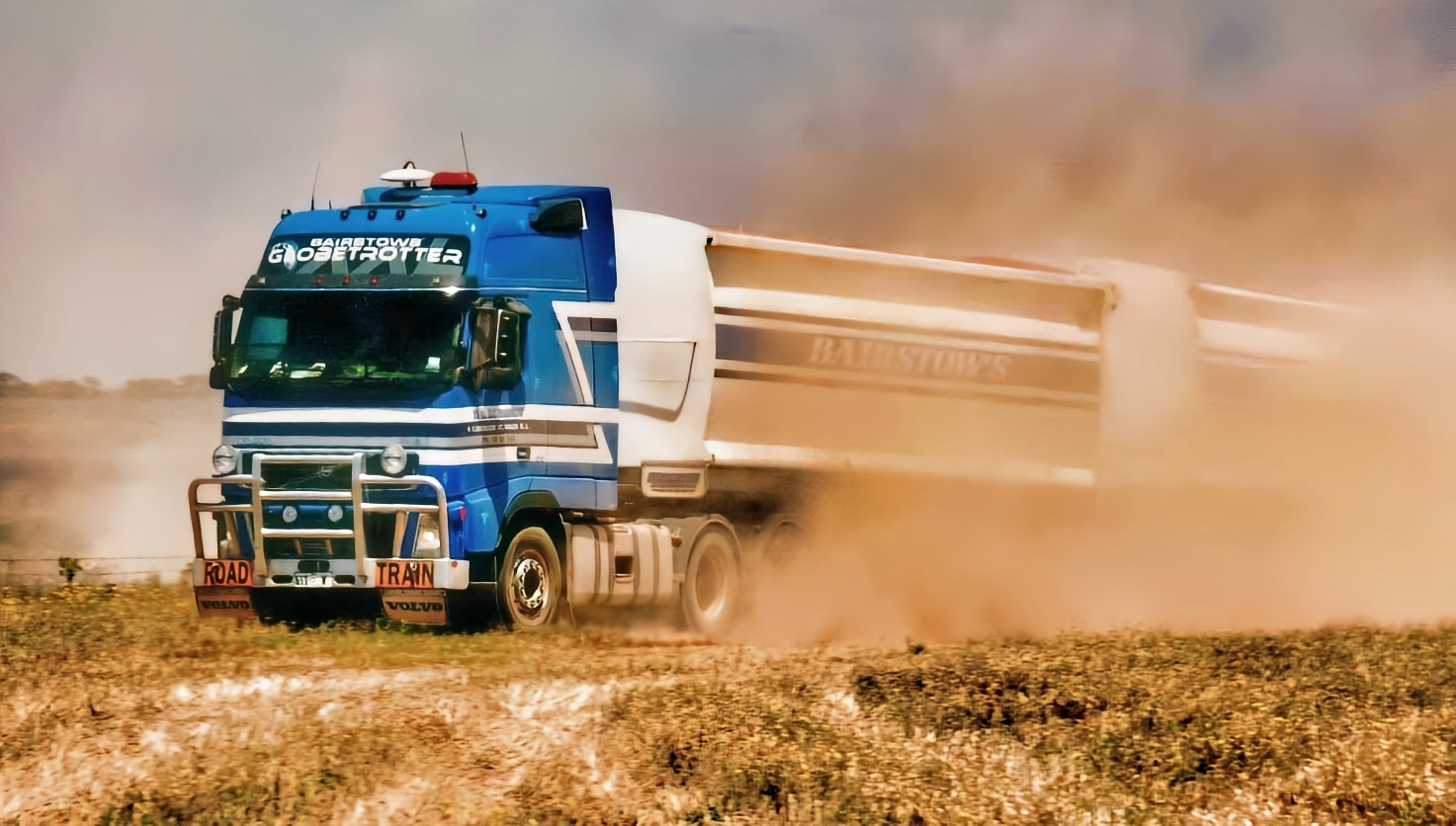 Un camión enorme atraviesa un prado levantando polvo