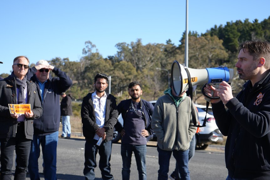 Man speaks to small assembled crowd through megaphone 