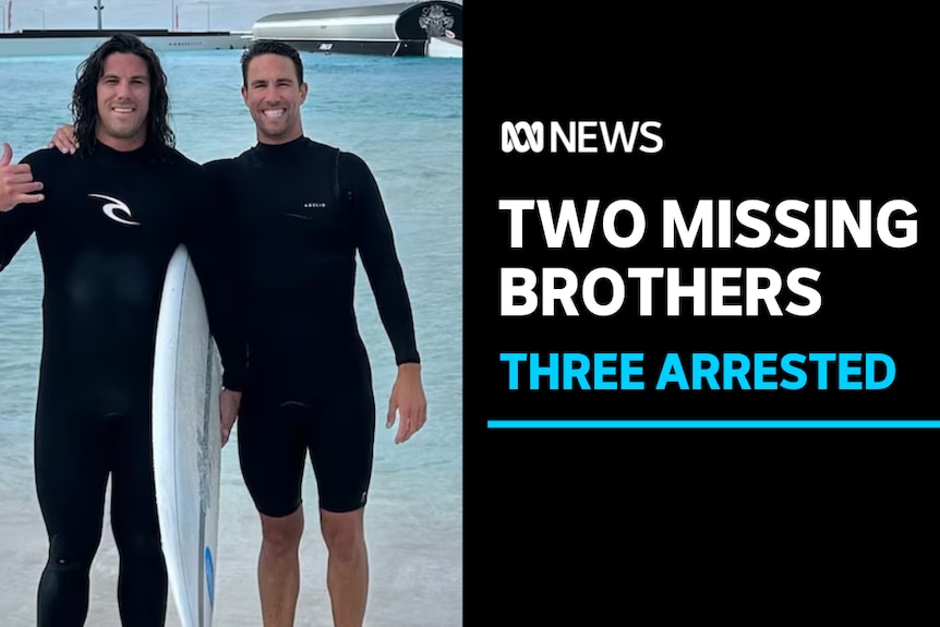Two Missing Brothers, Three Arrested: Two men in wetsuits pose on the beach. One holds a surfboard.