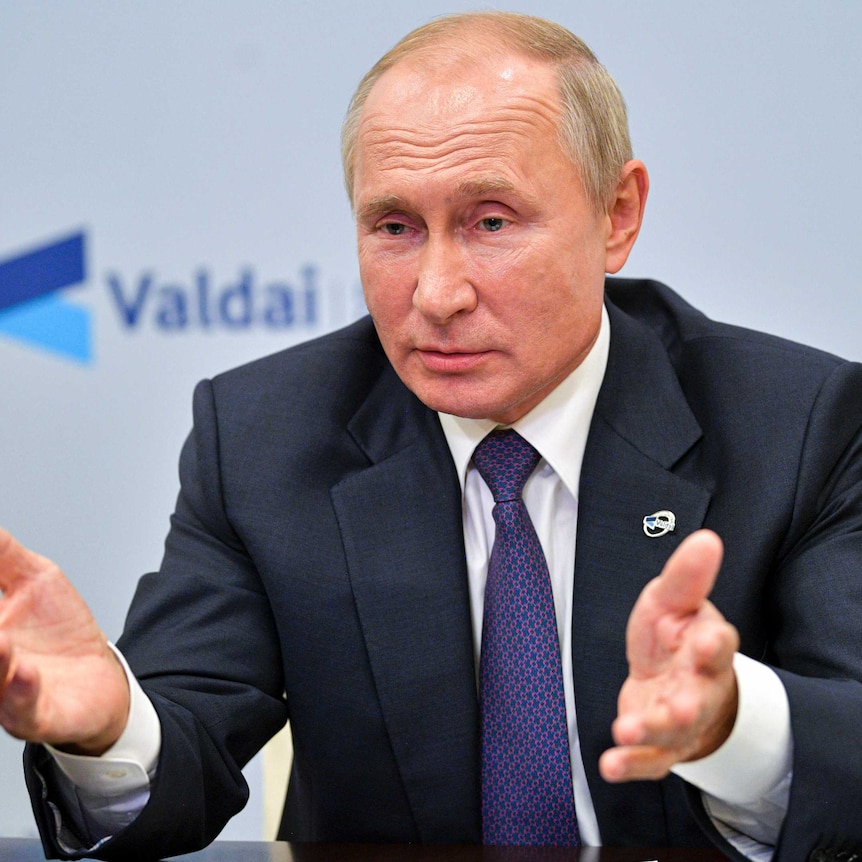 Russian President Vladimir Putin gestures while speaking from behind a desk wearing a suit and tie.
