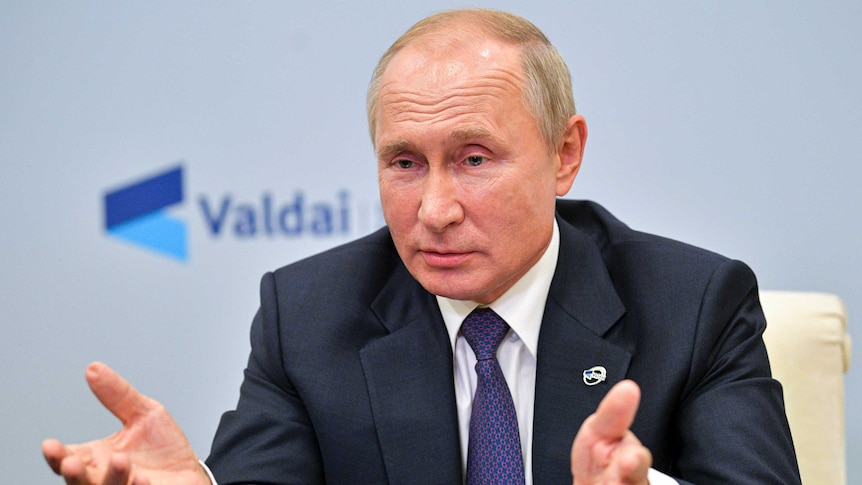 Russian President Vladimir Putin gestures while speaking from behind a desk wearing a suit and tie.