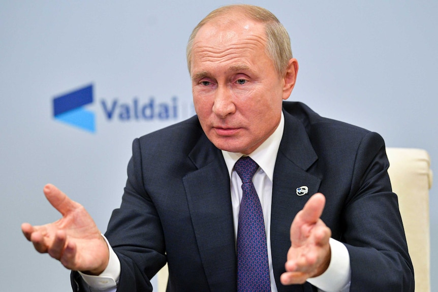 Russian President Vladimir Putin gestures while speaking from behind a desk wearing a suit and tie.