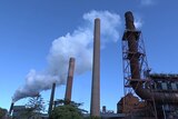Wide shot of a factory next to several towers emitting steam.