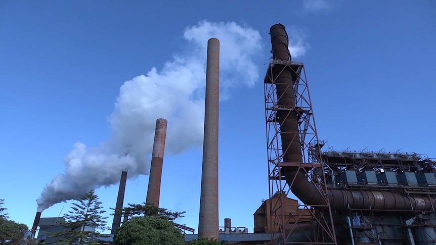 Wide shot of a factory next to several towers emitting steam.