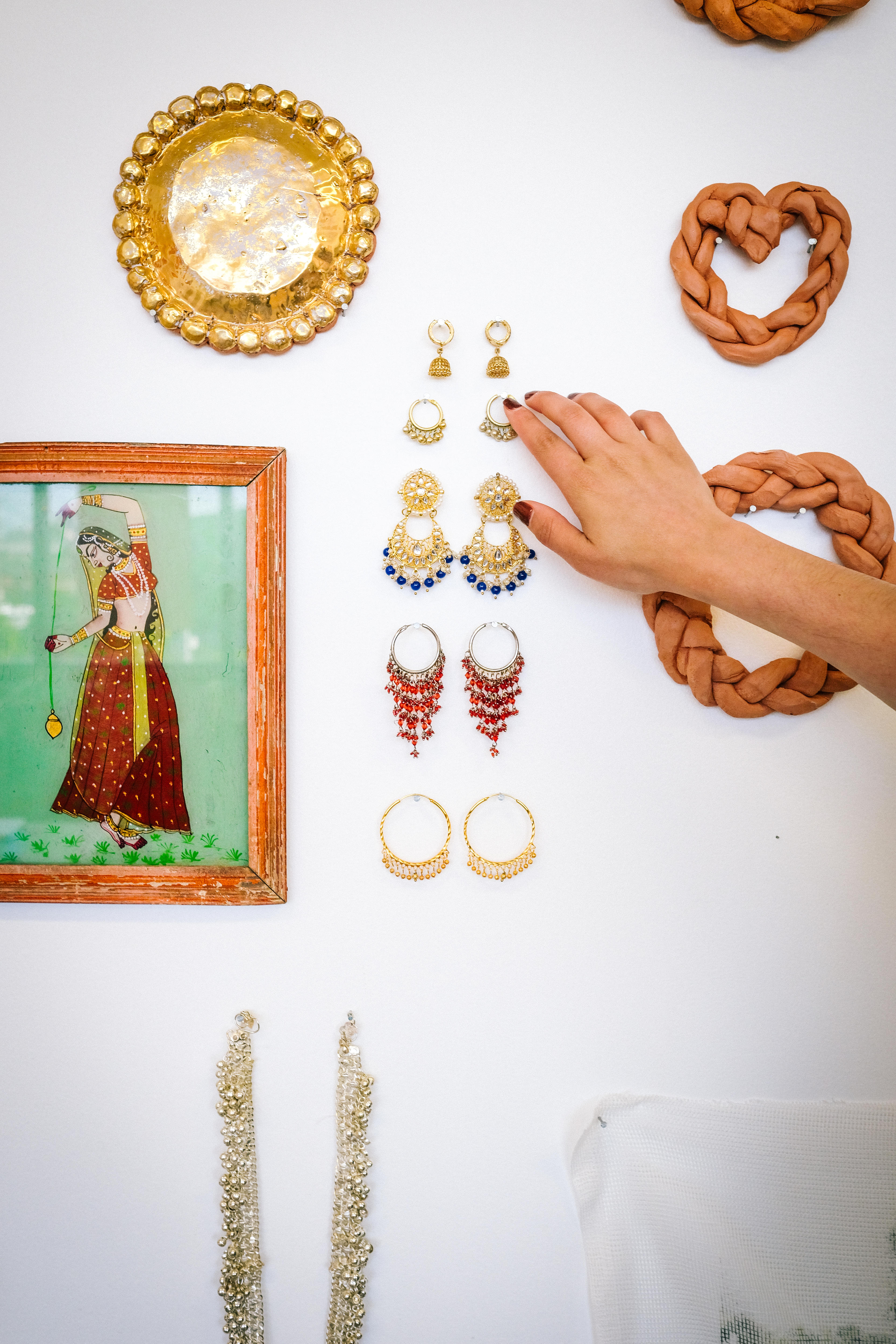 A detailed image of pairs of earrings pinned to the white studio wall — Rudhar's hand reaches out to touch them.