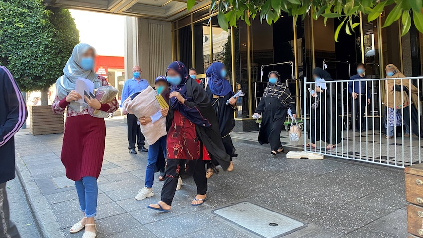 Women wearing headscarves walk out of the front doors of a hotel