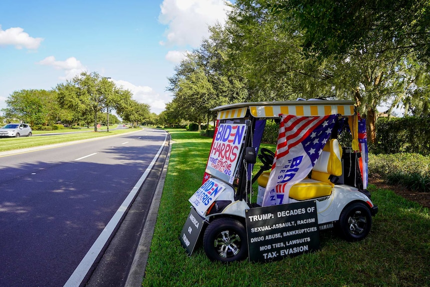 A golf cart parked on the side of the road covered in Biden-Harris campaign signs