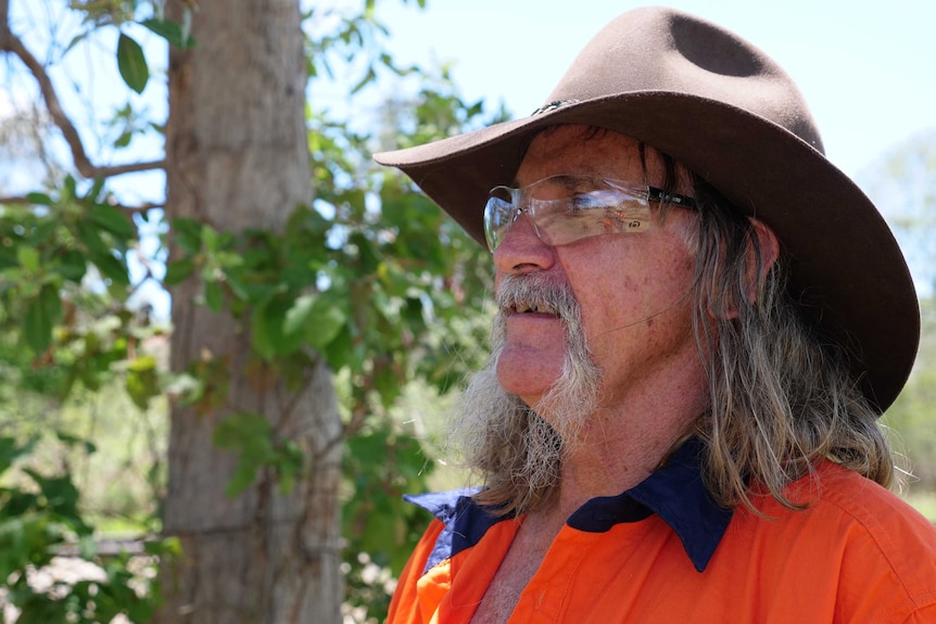 a man with a hat and safety glasses stands looking off to the distance