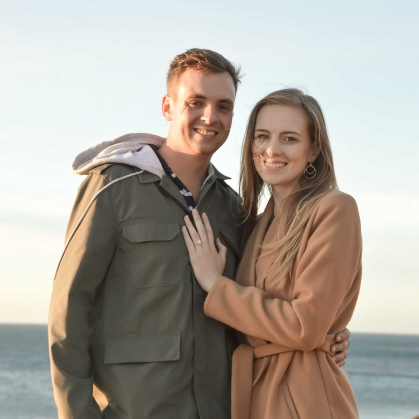 A man and woman standing by the ocean just after their engagement.