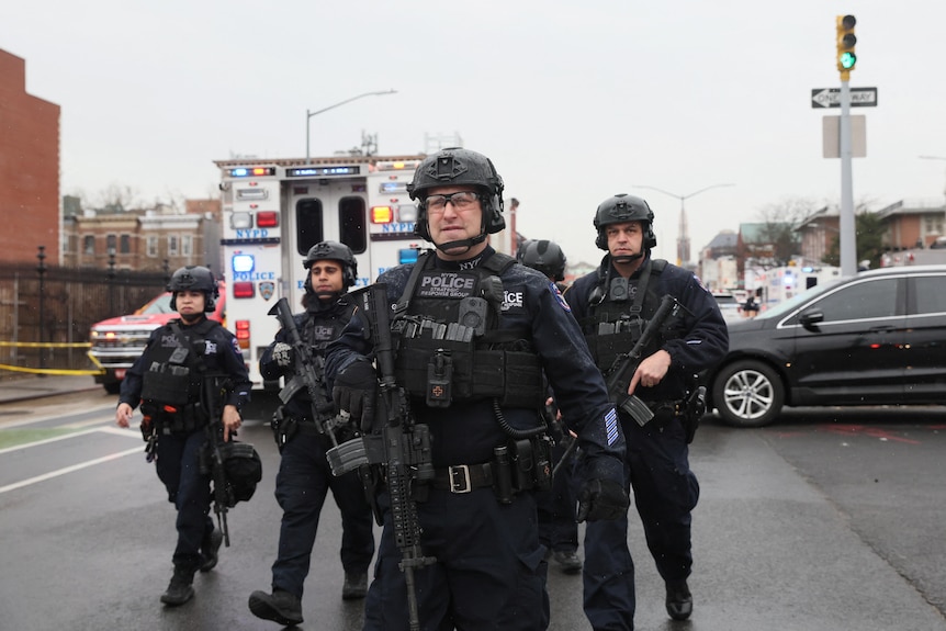 Police officers walk near the scene of a shooting at a subway station in the Brooklyn