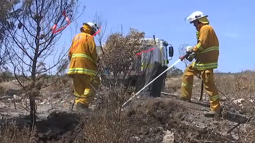 Two firefighters water down scrubland near a fire truck