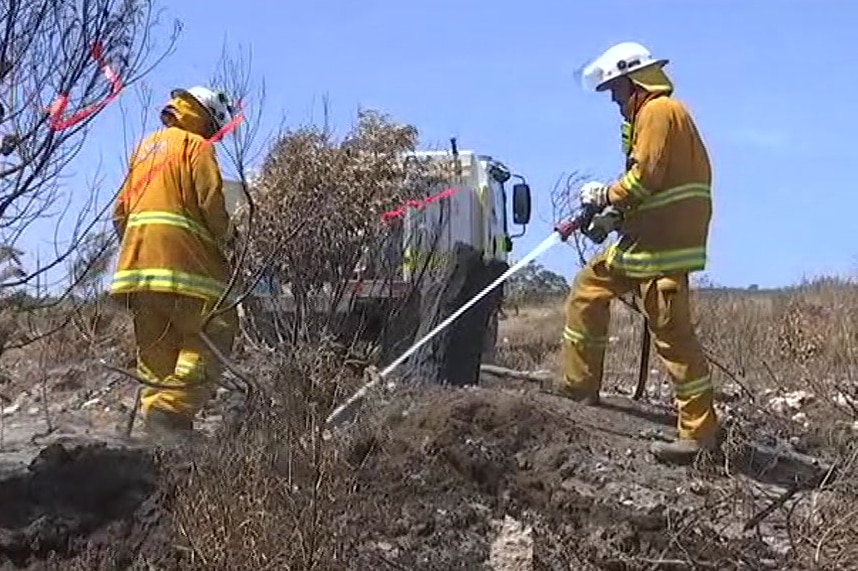 Two firefighters water down scrubland near a fire truck