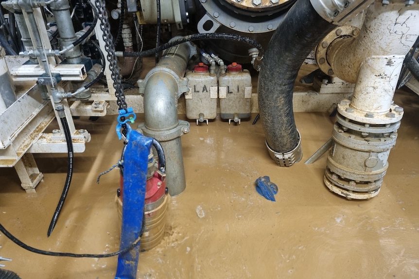 A number of pipes half-covered by muddy flood water.