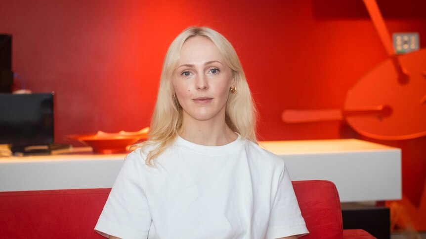 Laura Marling sits on the red triple j couch in a pristine white t shirt
