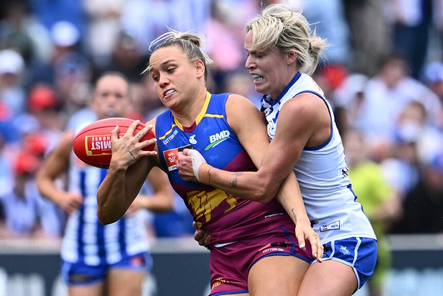 A Brisbane Lions AFLW player holds the ball as she is tackled by a Kangaroos opponent.
