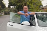 A man smiles while standing next to his car.