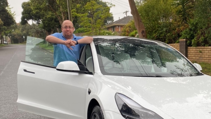 A man smiles while standing next to his car.