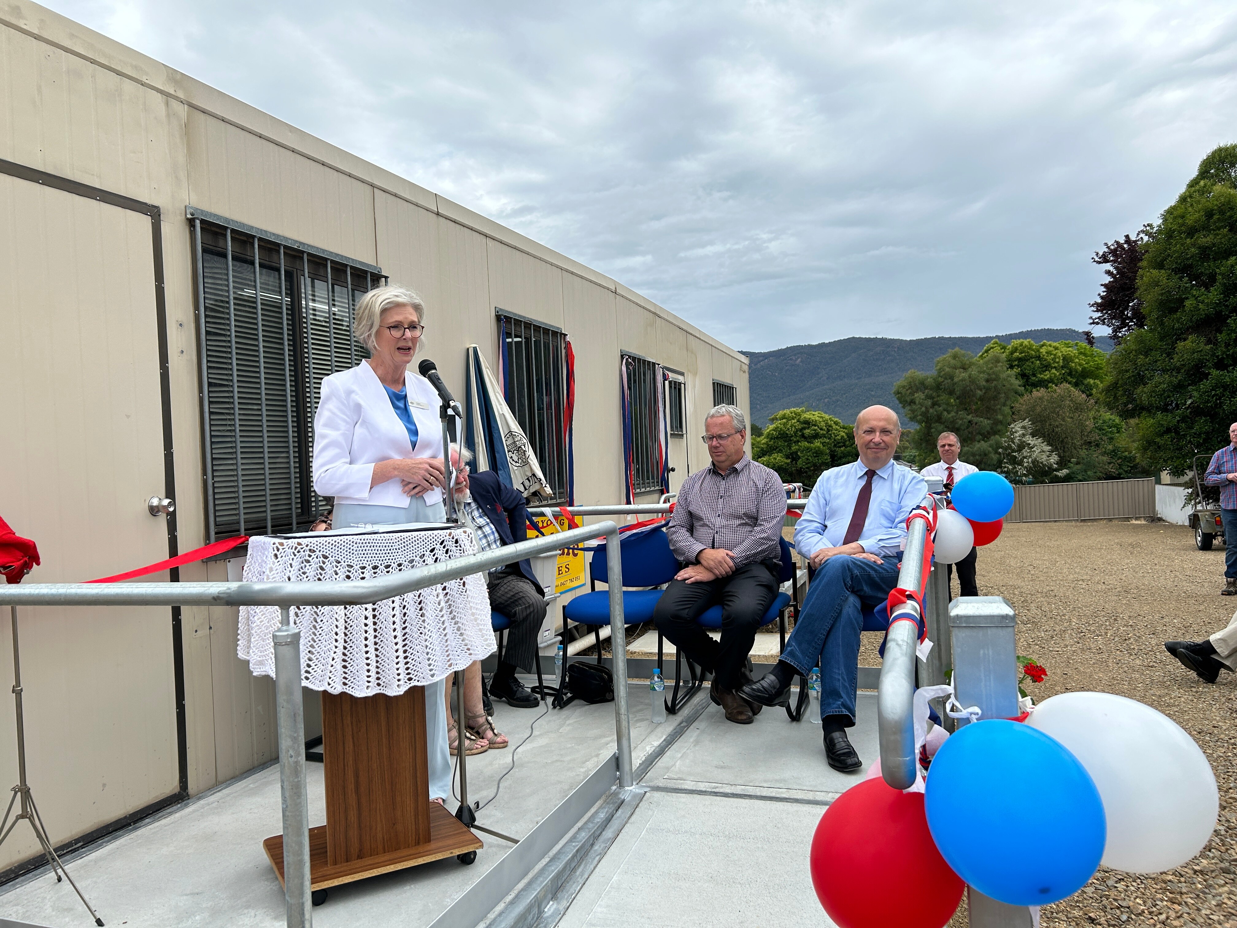 An image of MP Helen Haines speaking at the Corryong Foodshare opening, surrounded by celebratory balloons and mountain views.