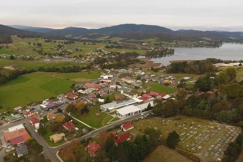 An aerial shot of a country town showing the main street, green fields and river