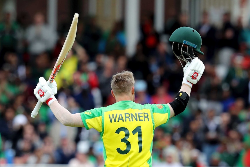 David Warner, back to the camera, holds his bat and helmet aloft.