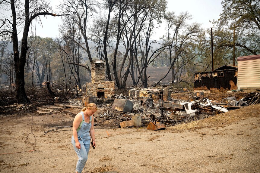 Une femme marche devant une structure détruite par un incendie. 