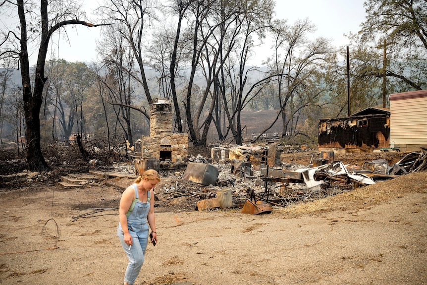 一名妇女走在被大火烧毁的建筑物前。 