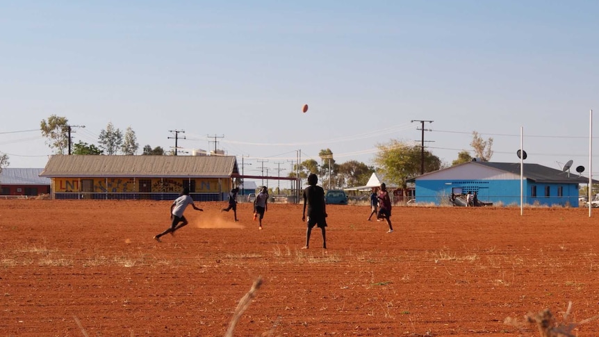 A group of boys play AFL on a red dirt oval