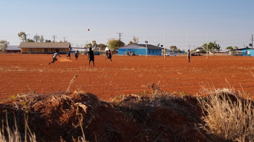 A group of boys play AFL on a red dirt oval