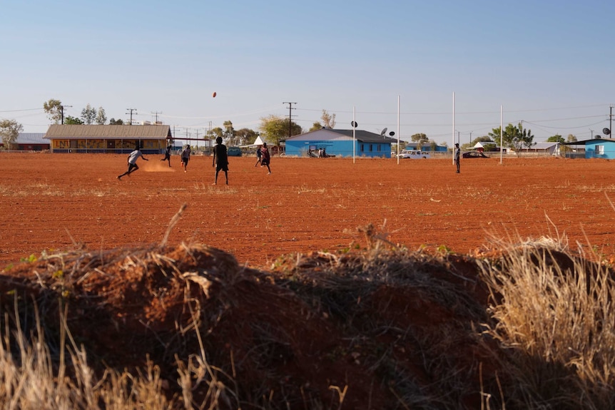 Un groupe de garçons joue à l'AFL sur un ovale de terre rouge