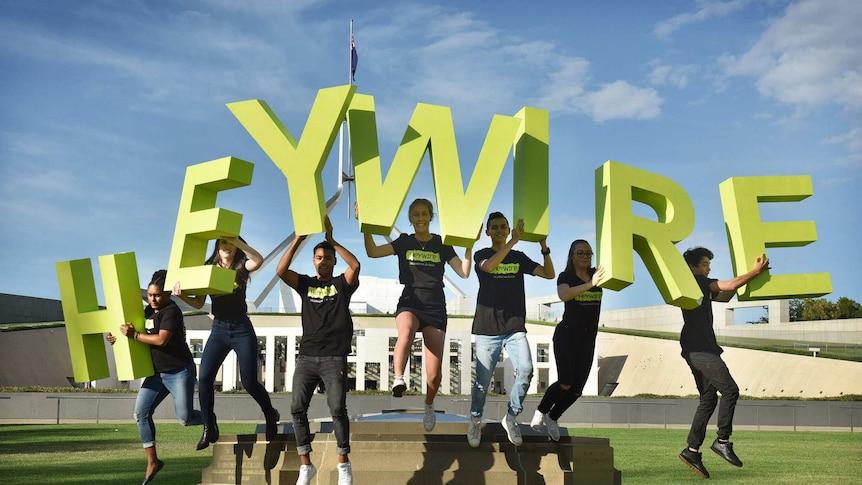 Young people in black t shirts standing outside the federal parliament holding letters spelling heywire
