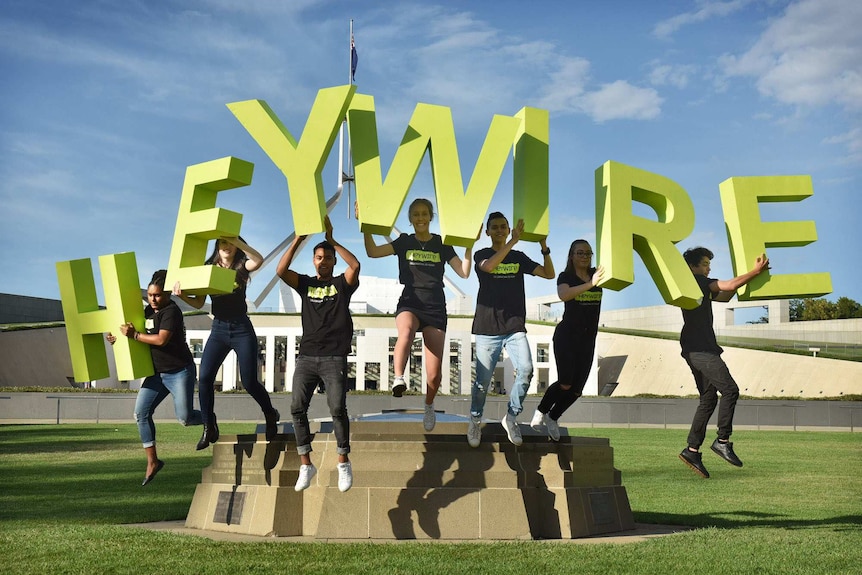 Young people in black t shirts standing outside the federal parliament holding letters spelling heywire