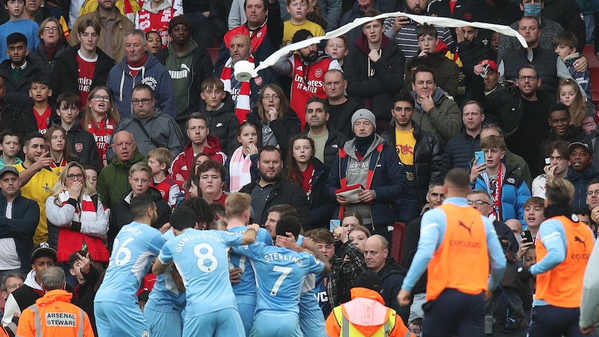 Arsenal fans look on as Manchester City players celebrate with a toilet roll being thrown towards them
