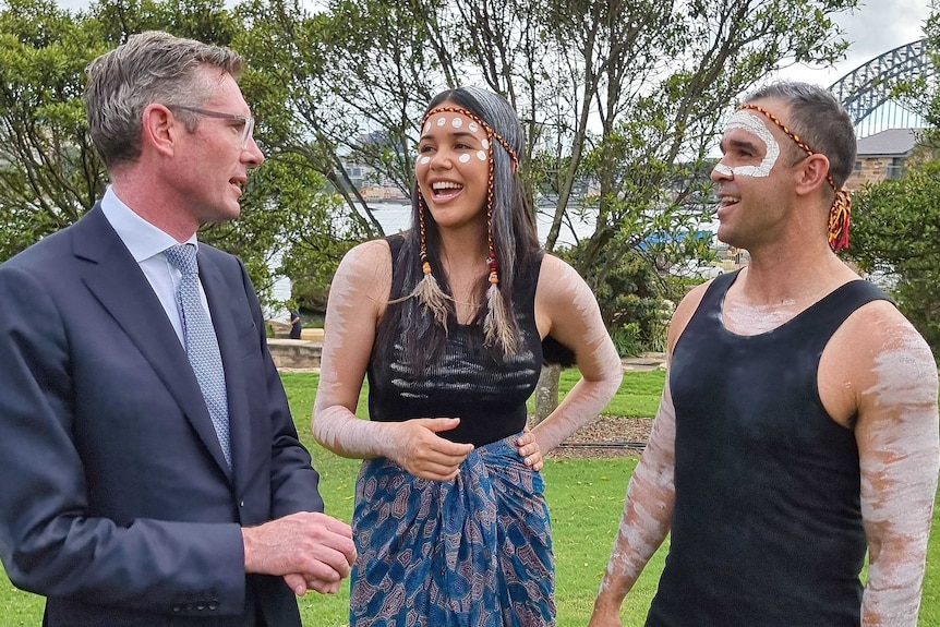 a man wearing glasses talking to two indigenous performers