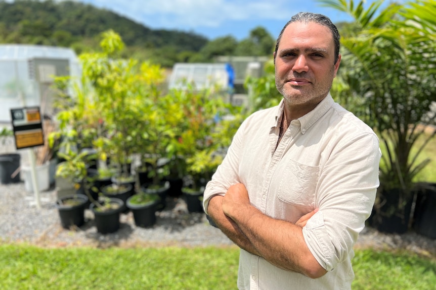 A profile of a man wearing a beige linen shirt in front of a collection of tropical potted plants