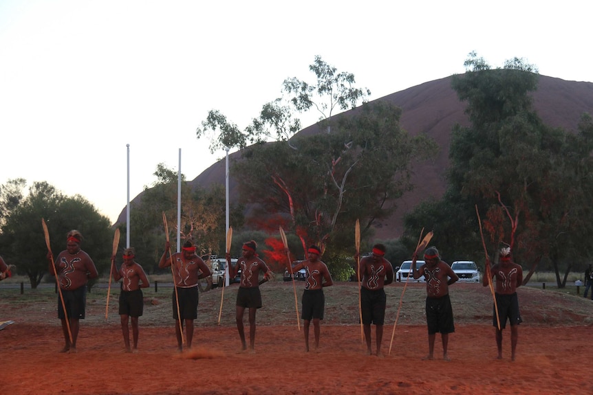 Eight dancers in traditional dress in front of Uluru.