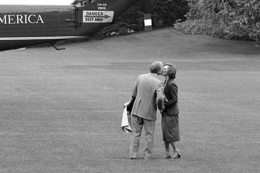 A black and white photo of Jimmy Carter kissing his wife on the lawn.