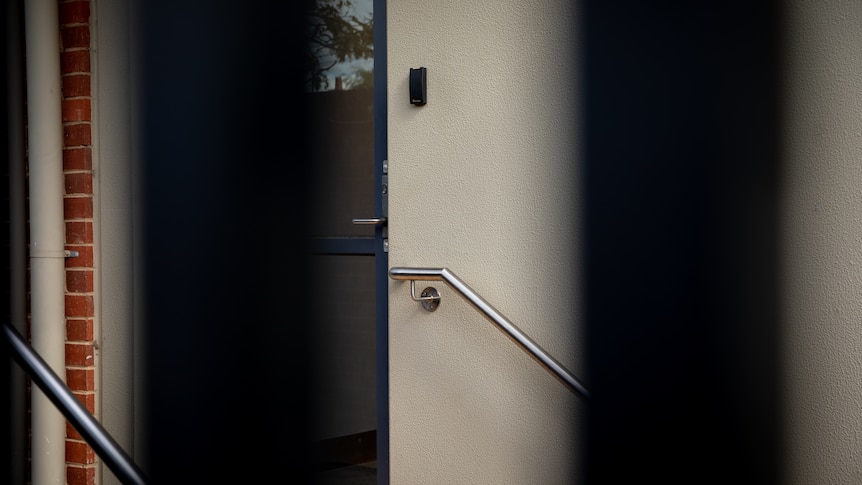 A closed door to a school building, viewed from between the bars of metal gates.
