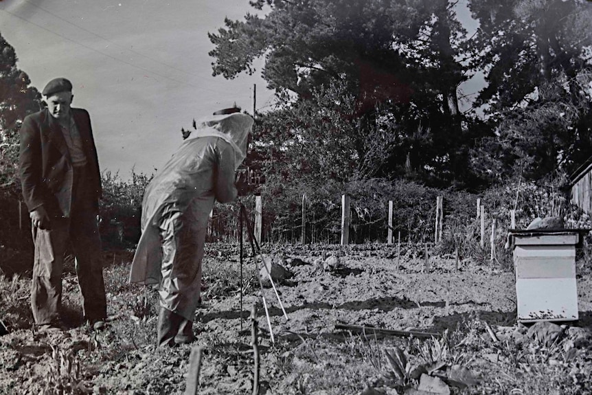 Black and white photo of woman with a camera on a tripod in a field