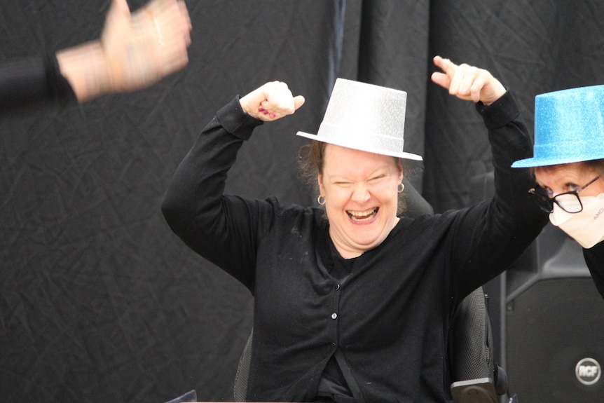 A performer with her arms in the air and a big smile, wearing a funny hat. Ausnew Home Care, NDIS registered provider, My Aged Care