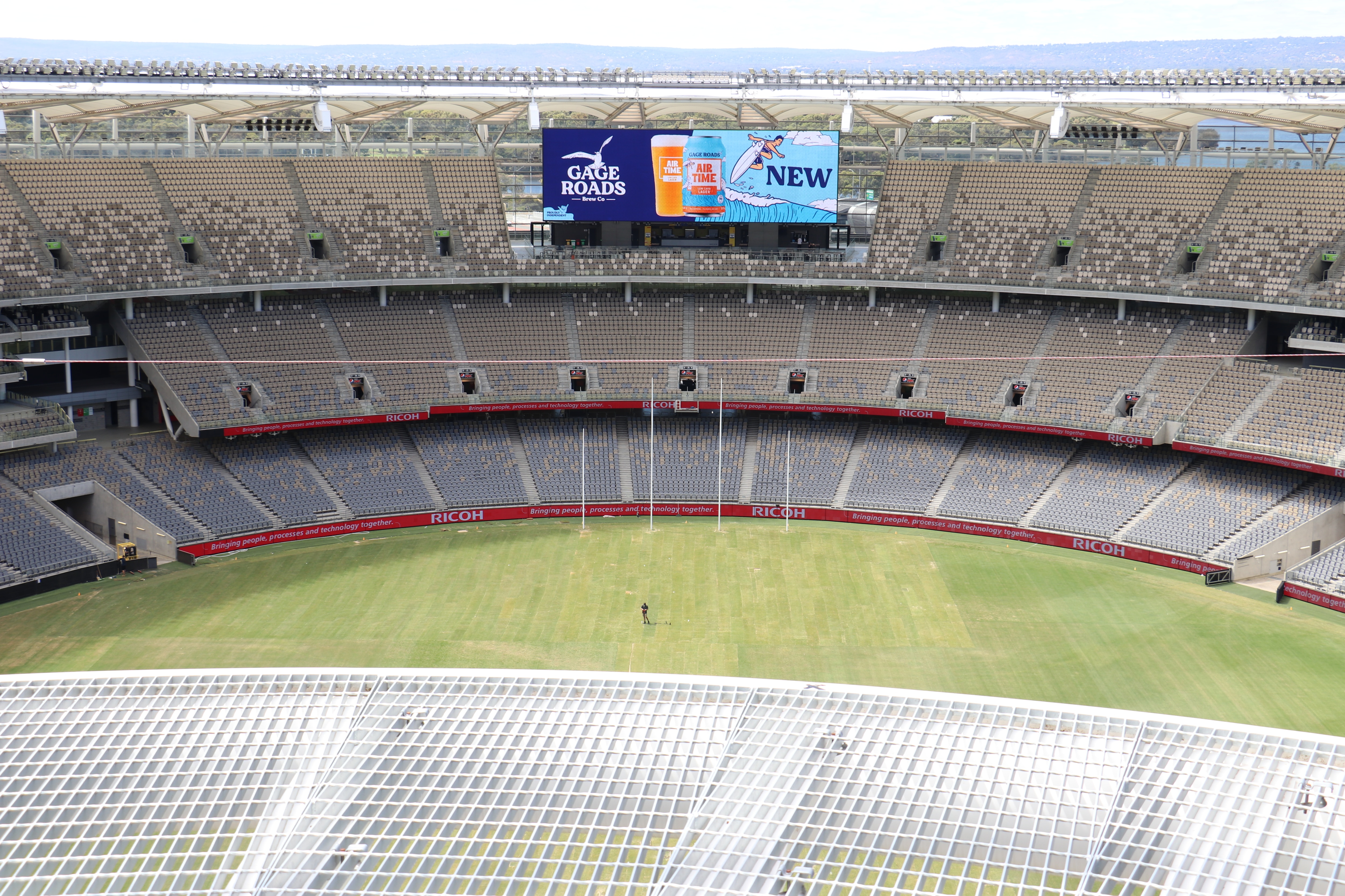 An empty stadium as seen from the roof, with one guy walking on the ground.