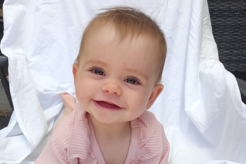 A baby on white sheets wearing pink