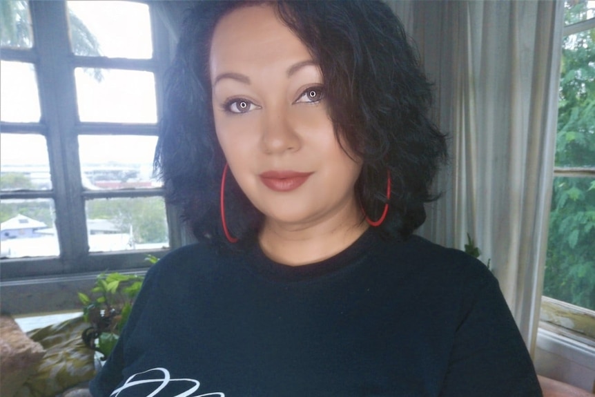 A woman with straight black hair and red hoop earrings giving a subtle smile to the camera. 